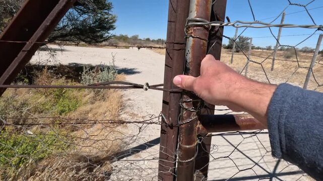 Metal gate in Africa. Man hand closes and opens metal fence gate.