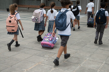 Obraz premium Group of primary school children walking into school with backpacks and rolling bags
