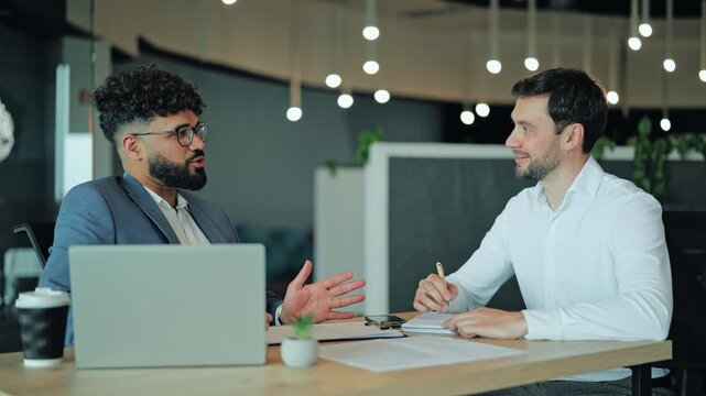 Friendly Middle Eastern businessman in glasses and suit speaking and smiling. Positive Arab professional manager, consultant, or IT developer communicating in contemporary workspace.