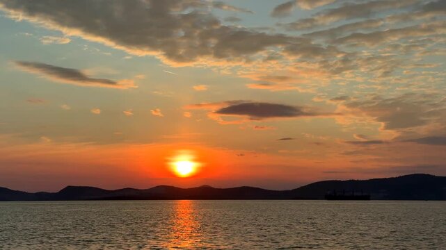 Beautiful golden sunset over the calm Aegean Sea in Gulluk, Turkey. The sun hangs low over distant mountain silhouettes, casting warm light on the rippling water.