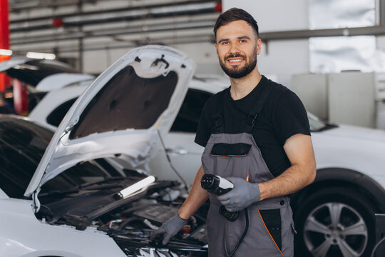 Car mechanic holding EV charging connector, smiling in a modern auto service, working on an electric car maintenance
