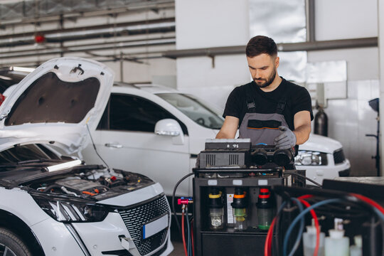 Young male mechanic performing vehicle maintenance, checking and recharging car AC system with professional machine