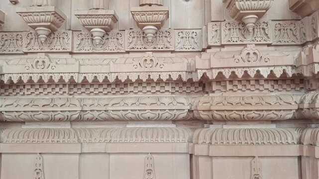 Tilt up shot of traditional female deities and intricate stone carvings on the pink sandstone wall of a Hindu temple