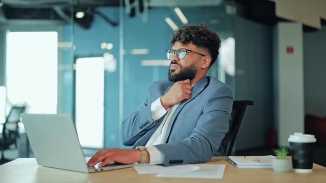 Middle Eastern businessman in a suit looking pained while touching his neck due to a severe sore throat. Image depicting illness, health problems, discomfort, and stress during a workday at office.