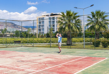 Fototapeta premium Adult man playing tennis on outdoor court during sunny day. Sport activity, fitness training, recreation, healthy lifestyle and leisure concept