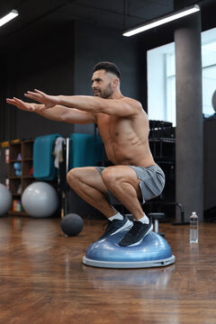 Fit athlete performing exercise on gymnastic hemisphere bosu ball in gym.