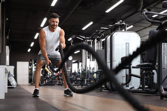 Athletic young man with battle rope doing exercise in functional training fitness gym.