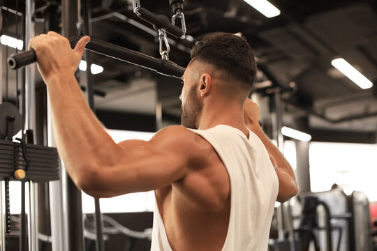 Fit and muscular man shakes his back on the simulator. Back view.