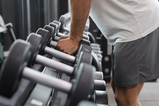 Fitness man in training showing exercises with dumbbells in gym.
