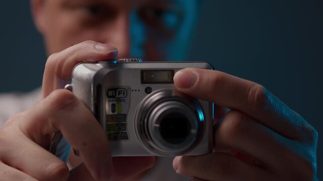 Amateur photographer holding old point and shoot digital camera, extending zoom lens and pressing shutter button to take picture, illuminated by moody blue and warm key lighting, close-up, slow motion