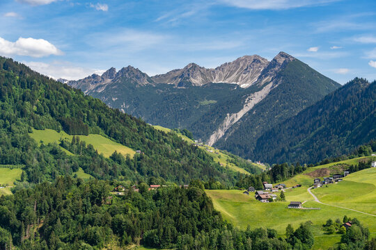 little village on a plateau in Grosswalsertal, in the middle of the mountains from Bregenzerwald. Panoramic view from an Austrian Alp to the spring-colored mountain