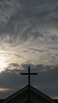 Church cross silhouette against dramatic cloudy sky at sunset, vertical shot