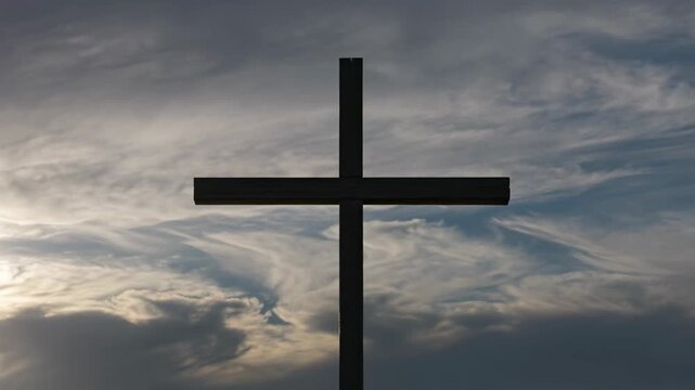 Silhouette of a wooden cross against a dramatic sky with swirling clouds and soft light breaking through