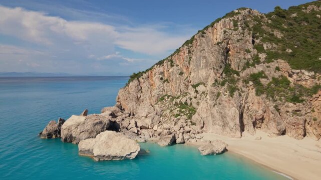 Aerial drone footage flying along dramatic coastal cliffs and massive sea rocks rising from crystal-clear turquoise water. Stunning Mediterranean coastline with rugged mountains, pristine sea, and bre