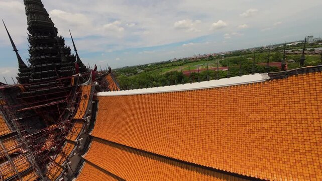 Aerial FPV rising shot of tall black spire on top of Wat Man Buddhist temple in Thailand as a flock of birds fly away