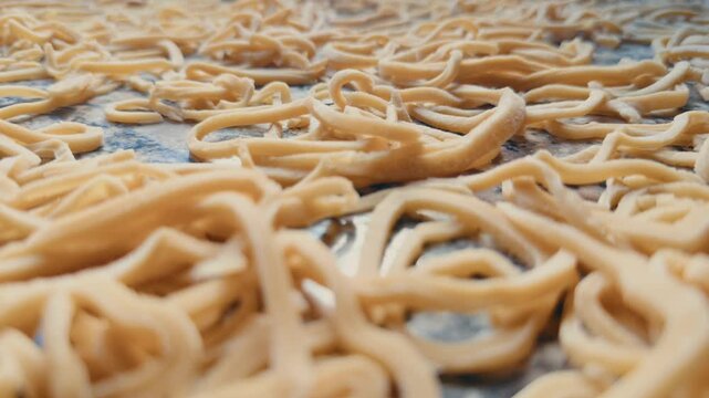 Close-up dolly shot moving left to right over freshly made homemade egg noodles spread across a kitchen countertop for drying. Traditional pasta preparation, artisan cooking.