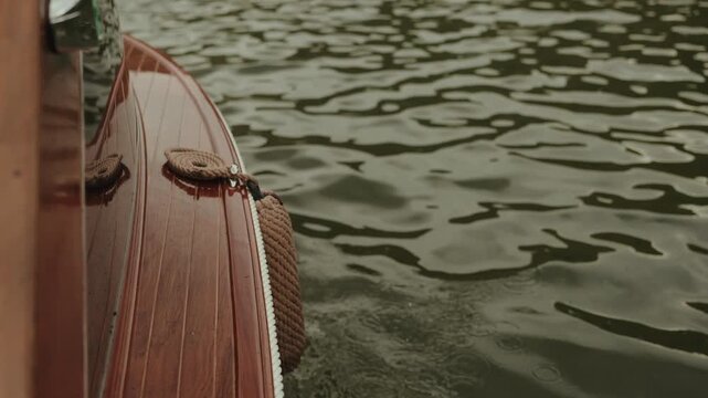 neatly coiled marine rope on the polished wooden deck of a cruising boat, with a fender hanging over the rippling river water