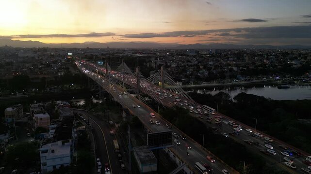 Heavy traffic crossing Puente Duarte and Juan Bosch bridge over Ozama river with sunset sky in Santo Domingo, Dominican Republic. Aerial drone, cityscape