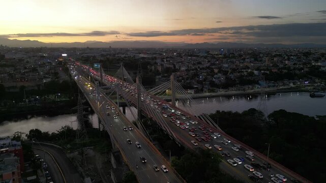 Drone view of heavy traffic on Juan Pablo Duarte and Juan Bosch bridge over Ozama river at dusk in Santo Domingo, Dominican Republic. Aerial backward