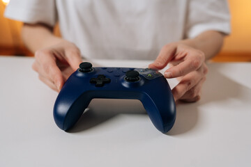 Person hands placing navy blue wireless video game controller on white table, ready for playing video games and immersing in digital entertainment and leisure time, close-up. © dikushin