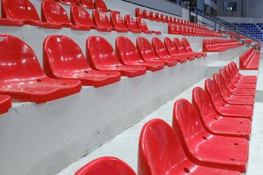 Rows of empty red plastic seats in a stadium tribune.