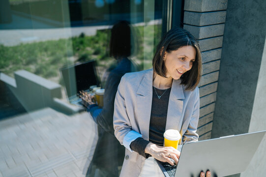 Smiling businesswoman working on laptop with coffee outdoors