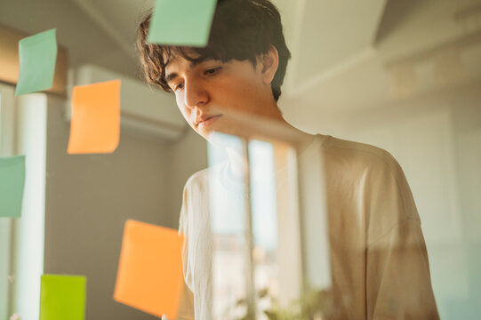 Teenager brainstorming with notes on glass window in the office