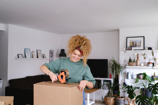 Smiling woman packing box with adhesive tape
