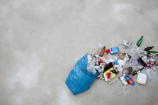 Garbage spilling from plastic bag on gray background