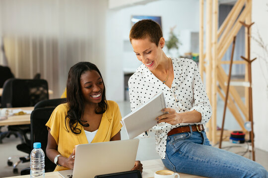 Smiling colleagues with laptop and notepad working together at desk in office