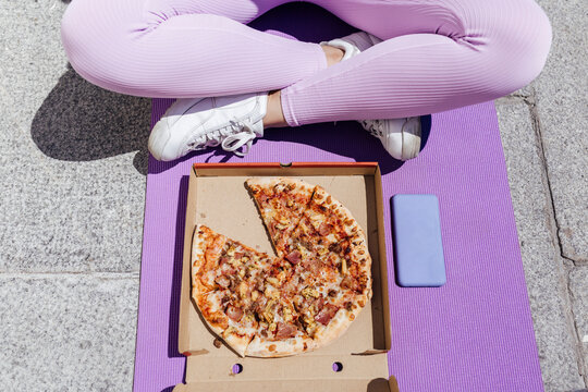 Female athlete sitting cross-legged in front of pizza on exercise mat