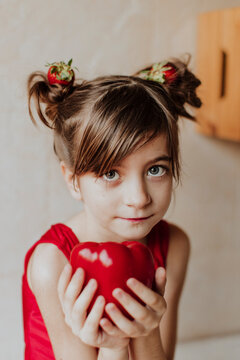 Child with strawberry pigtails holding a red pepper indoors
