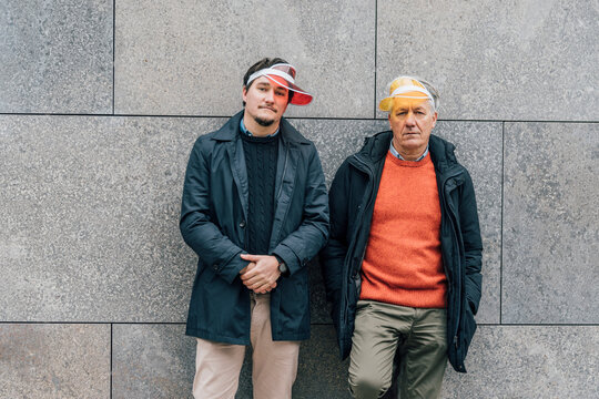 Portrait of young man and senior man wearing sun visors leaning against a wall