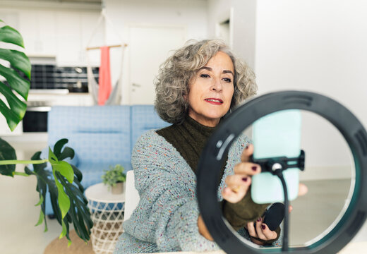 Senior woman adjusting smart phone in ring light for filming at home