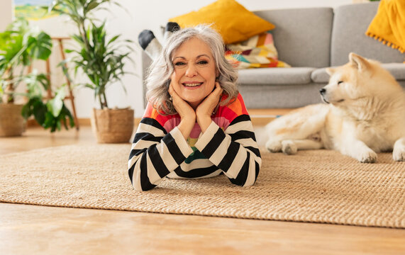 Smiling mature woman lying on carpet with dog in background