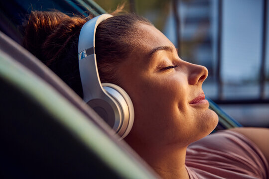 Smiling young woman lying on hammock on balcony listening music with headphones