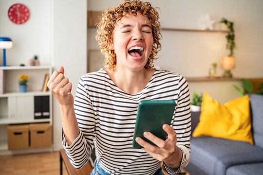Joyful woman celebrating mobile success indoors with striped shirt