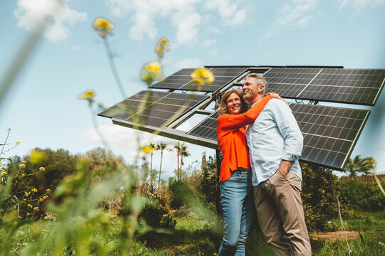 Mature woman hugging man standing in front of solar panels