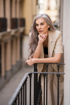 Elegant woman with grey hair leaning on a city balcony