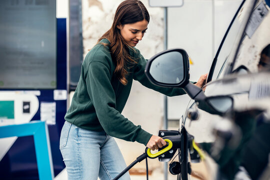 Smiling woman plugging charger in car at electric vehicle charging station