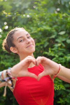Smiling student making heart shape with hands in garden