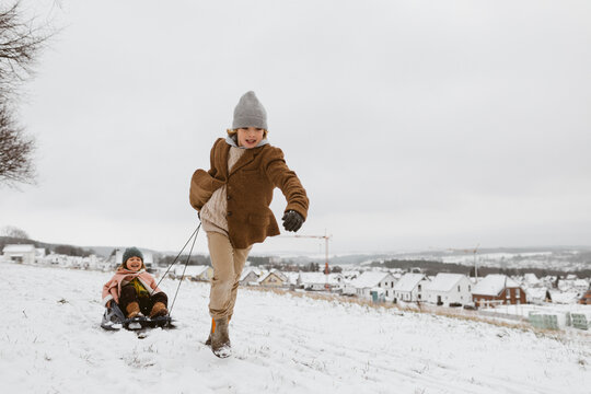 Boy pulling sledge with little sister in snow
