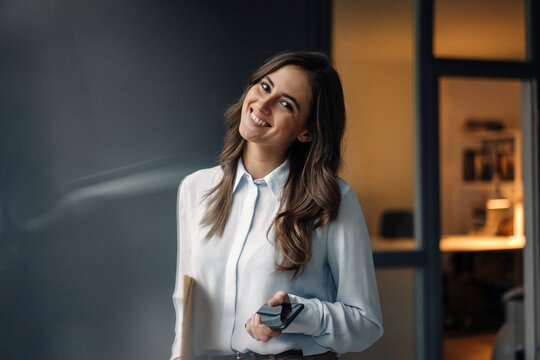 Portrait of smiling young businesswoman holding folder and cell phone