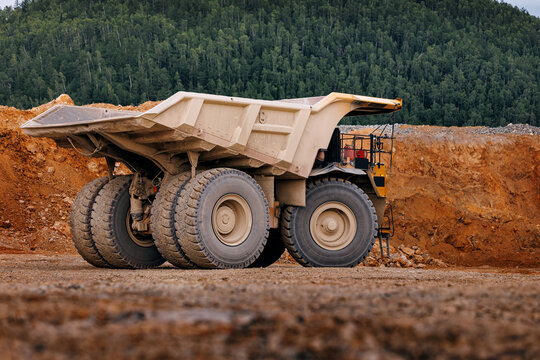 Massive mining dump truck parked at quarry edge with forest backdrop for heavy equipment background and industrial design