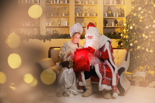 Ded moroz and snegurochka celebrating christmas with gifts in festive setting. Russian Father frost and Snow Maiden with sunlight bokeh