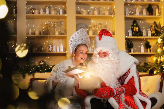 Happy Ded moroz and snegurochka sharing gifts in festive holiday setting. Russian Father frost and Snow Maiden with sunlight bokeh