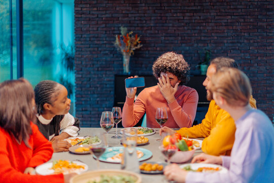 Man showing smartphone feeling embarrassed at dinner party