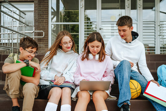 Pupils doing homework using laptop sitting on steps