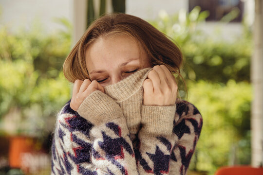 Portrait of young woman with closed eyes sinking in her woolen sweater