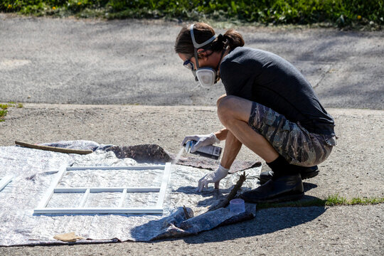 Painter crouching outdoors spraying paint on a window frame